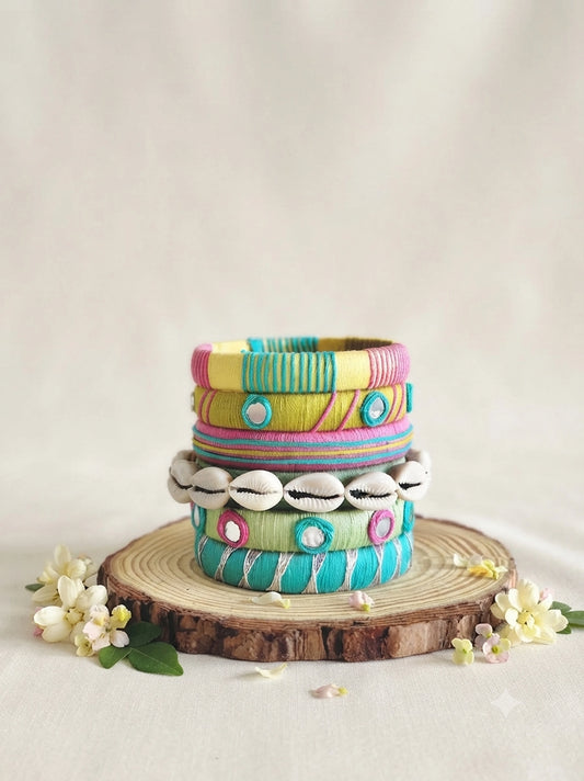 Aadhya Bangles — Multicolor thread bangles with mirror work, silver bells, kundan stones, silver charm ghungroo, parrot motifs, cowrie shells, and pom-poms.